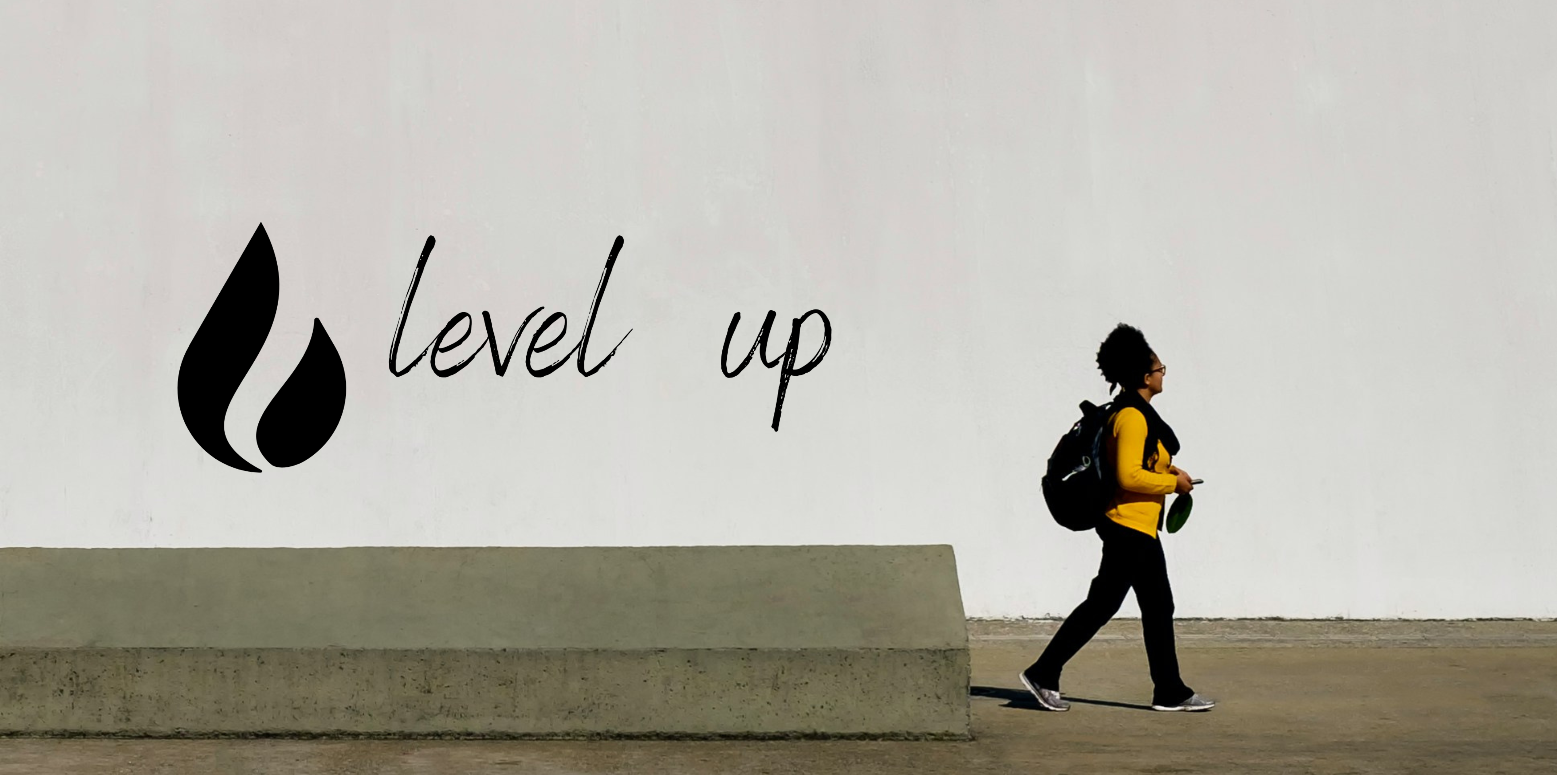 Girl wearing a yellow jacket walking toward the right of the frame. She has a backpack on. In the background is a concrete wall with a logo on the left that reads "level up".